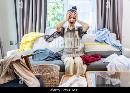 A woman having a headache because of the messy laundry all over the room Stock Photo