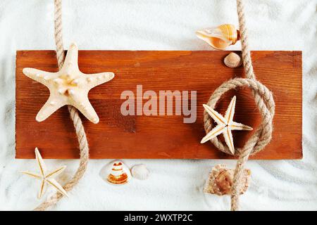 Seashells, starfish, rope and wooden board on the sand. Summer background, copy space, template, flat lay. Stock Photo