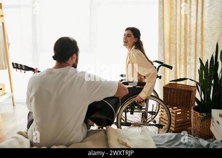 joyful woman with disability in wheelchair watching her bearded husband playing guitar for her Stock Photo
