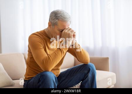 Elderly man sitting on sofa with head resting on hand Stock Photo