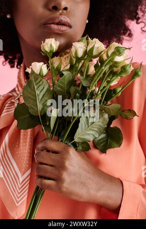 cropped view of african american girl in peach fuzz blouse holding flowers on pink backdrop Stock Photo