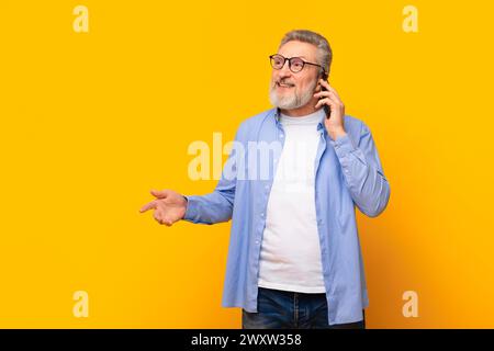 Cheerful senior man talking on cell phone on yellow background Stock Photo