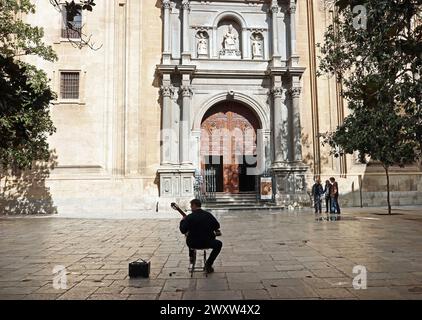 A classical Spanish guitarist silhouetted in dappled sunlight busks in a square in front of the Cathedral in Granada, Andalusia, Spain Stock Photo