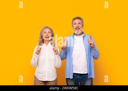 Excited senior couple pointing fingers up at free space, studio Stock Photo