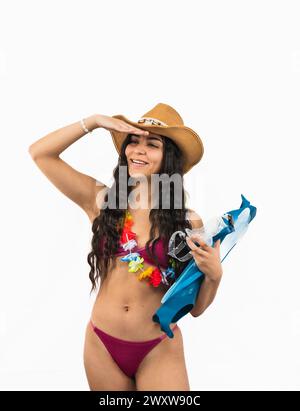 young Latin woman wearing a bikini holds diving fins while shielding her eyes from the summer sun with her hand on white background Stock Photo