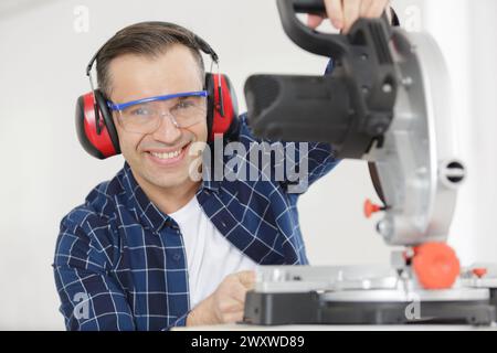 happy workman cutting wooden planks using circular saw in workshop Stock Photo