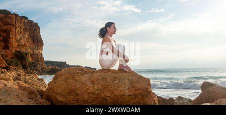 woman sitting on a rock by the sea, looking thoughtful Stock Photo
