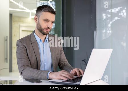 Focused mature male professional using computer in a contemporary workspace setting, displaying serious concentration. Stock Photo
