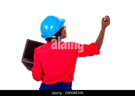 beautiful adult female engineer wearing blue safety helmet writing on a whiteboard with a mark using a laptop. Stock Photo