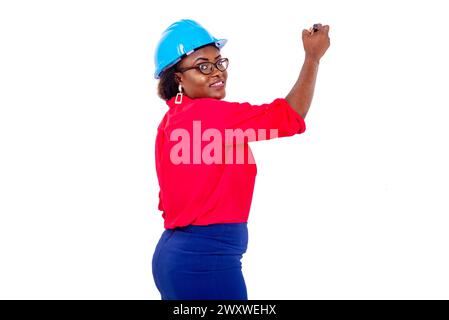 beautiful adult female engineer wearing blue safety helmet writing on a whiteboard with a mark while smiling. Stock Photo