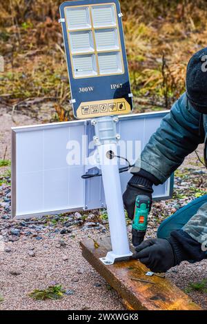 Installing completely self-contained, stand alone solar-powered LED street light, an electrician mounts holder bracket to wooden pole. Stock Photo