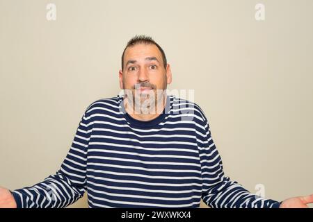 Hispanic man with beard in his 40s isolated on beige background doubting and shrugging shoulders in questioning gesture Stock Photo