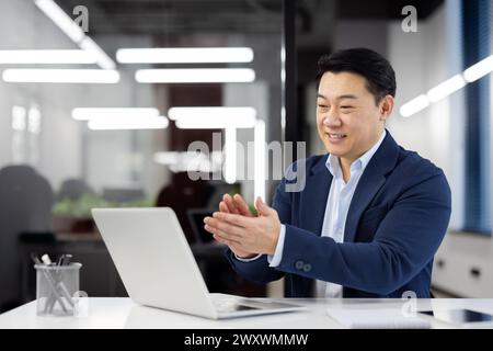 Professional businessman clapping hands while participating in an online video call with colleagues in a modern office setting. Stock Photo