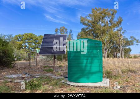 Large green plastic storage tank with solar panes connected to a borehole. Concept for extracting groundwater in locations where pumped water and elec Stock Photo