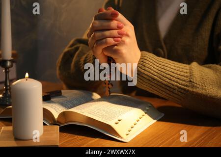 Woman praying at table with burning candle and Bible, closeup Stock Photo