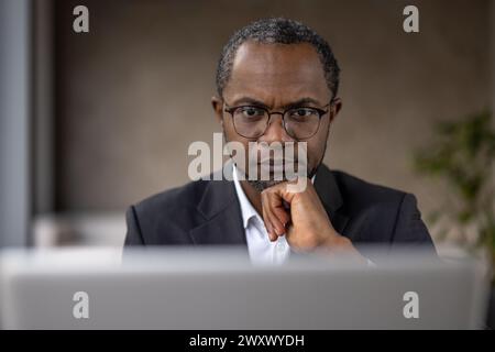 A concentrated African-American businessman in office attire working intently on his laptop, displaying professionalism and dedication. Stock Photo