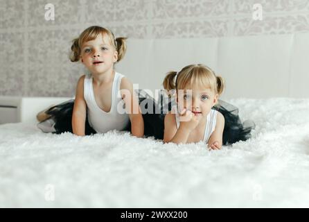 Two young girls are laying side by side on a bed, looking towards the camera with a neutral expression. Stock Photo