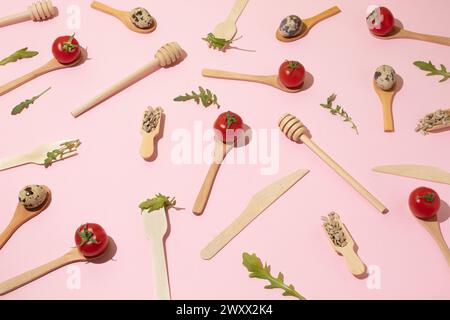 Wooden kitchen cutlery, cherry tomatoes, quail eggs, sunflower seeds on pink background. Flat lay pattern Stock Photo