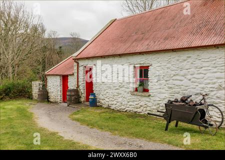 Traditional red painted irish cottage with a wheelbarrow of peat and a bicycle outside Stock Photo