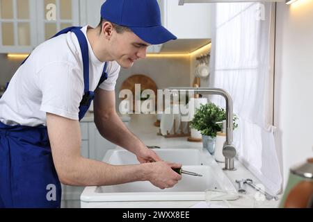Smiling plumber repairing sink with screwdriver in kitchen Stock Photo