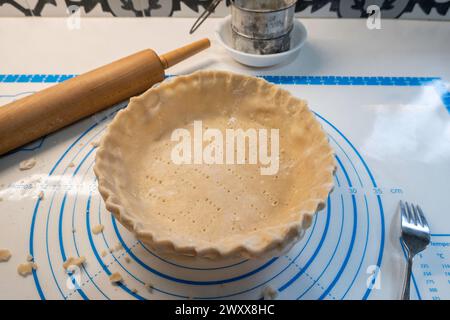Pie crust or pastry rolled out and fitted into a pie plate. Flour sifter & wooden rolling pin visible. Stock Photo