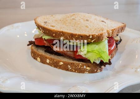 BLT, Bacon, lettuce & tomato sandwich  with oatnut bread & mayo on a white plate. Stock Photo