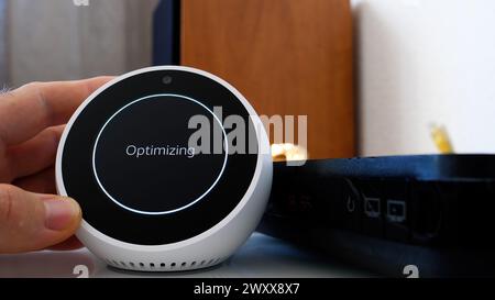 Paris, France - Jun 5th, 2020: A person holding Amazon Alexa smart device with the word optimizing on the screen, implying the action of improving performance or efficiency on the device. Stock Photo