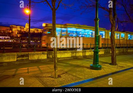 Enjoy the evening city walk down Jane Haining embankment of Danube with a view of riding vintage tram and Buda Castle atop the Castle Hill in backgrou Stock Photo