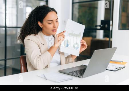 Financial online consultation. Successful brazilian or hispanic businesswoman, financial top manager, showing financial report her colleagues by online video conference, discussing strategy, smiling Stock Photo