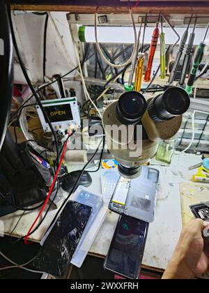 Perak,Malaysia. April 2,2024: Mobile technician inside his workshop repairing and servicing the customer hand-phone at Mas Headphone Repair  shop. Stock Photo