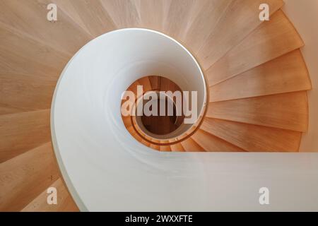 An overhead view of a contemporary spiral staircase with a flawless white balustrade and warm wooden steps that elegantly twist downwards. Stock Photo