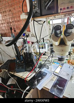 Perak,Malaysia. April 2,2024: Mobile technician inside his workshop repairing and servicing the customer hand-phone at Mas Headphone Repair  shop. Stock Photo