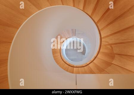 An overhead view of a contemporary spiral staircase with a flawless white balustrade and warm wooden steps that elegantly twist downwards. Stock Photo