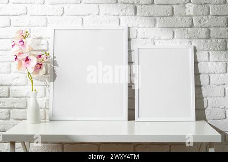 Two Blank Photo Frames on a White Table Against a Brick Wall With Orchids in Vase Stock Photo