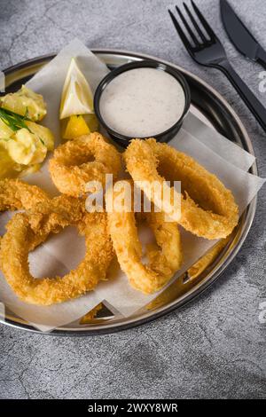 Fried calamari with potato salad next to it on stone table Stock Photo