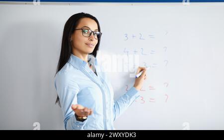 Woman teacher standing at blackboard with formulas and explaining information Stock Photo