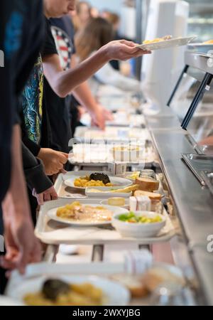 Lunchtime in the canteen of the junior high school “college de La Voulte” (south-eastern France): students carrying trays with meals Stock Photo