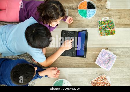From above children are seen from above playing with hama beads and using a laptop, illustrating a blend of traditional crafting and digital learning Stock Photo