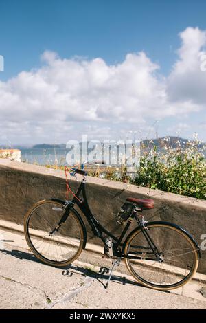 A classic black bicycle with a leather saddle rests against a sea wall, overlooking the scenic San Francisco Bay in springtime Stock Photo