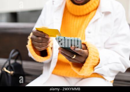 Close-up cropped unrecognizable of African woman using her mobile phone while holding a credit card in an urban environment Stock Photo