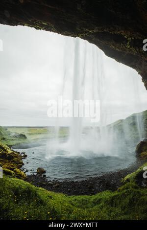 Verdant Icelandic landscape showcasing a magnificent waterfall cascading down with a unique view from behind the water curtain. Stock Photo