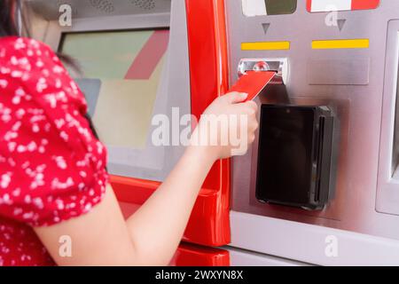 Close-up view of a woman's hand inserting a red debit card into an automated teller machine Stock Photo