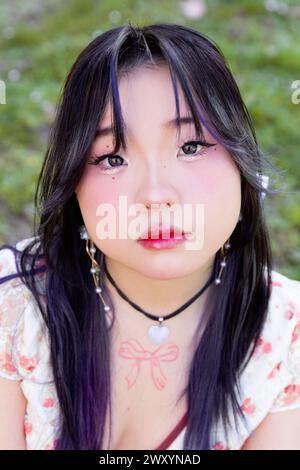 A close-up image of a young Asian Chinese woman with subtle makeup, looking intently at the camera with a natural green background. Stock Photo
