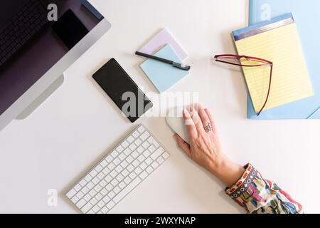 Anonymous person in a secretariat with a computer, smartphone, and various stationery items, capturing the feeling of a professional workspace Stock Photo