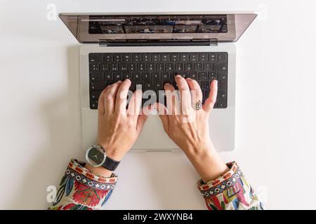 From above of anonymous person hands are shown typing on a sleek laptop keyboard, accessories hint at a stylish professional setting Stock Photo