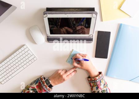 Top view of anonymous hand of well-organized desk featuring a digital tablet, keyboard, mouse, and various office supplies, with hands taking notes on Stock Photo
