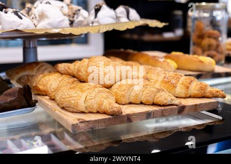 Golden, freshly baked croissants artfully arranged on a rustic wooden board in a bakery's glass display case Stock Photo