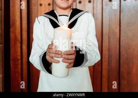 A close-up of anonymous child's hands tenderly holding a lit candle, a symbol of faith during the First Communion celebration Stock Photo