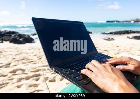 Close-up of anonymous hands typing on a laptop against a stunning beach backdrop, showcasing a digital nomad's mobile office Stock Photo