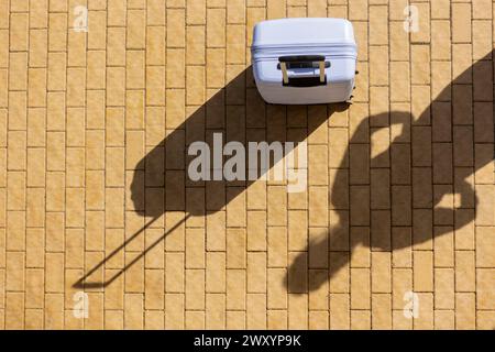 Overhead view of a suitcase casting a long shadow on a yellow brick ground, symbolizing travel and airports Stock Photo
